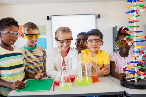 a number of children at a science lab table with colorful beakers and safety glasses